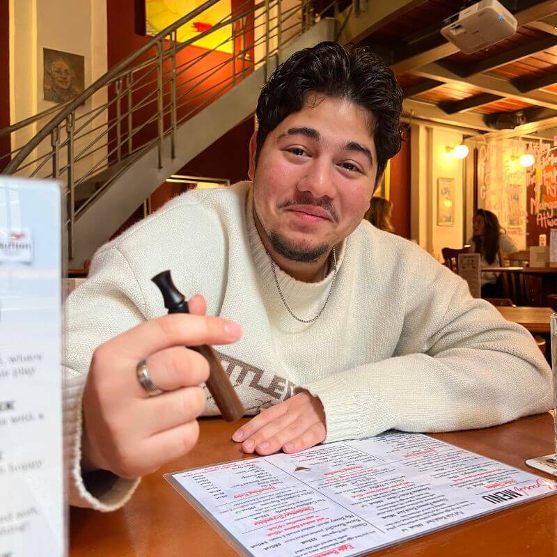 Person sitting at a restaurant table, holding a vape pen.