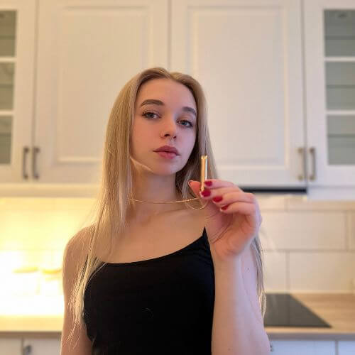 A person in a kitchen holding a necklace, wearing a black top.