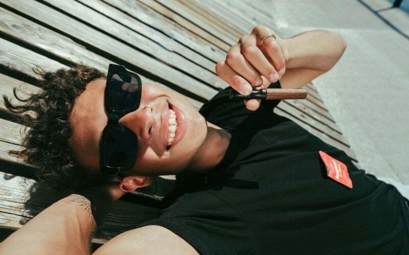 Person lying on wooden deck, wearing sunglasses, smiling, holding a small object.