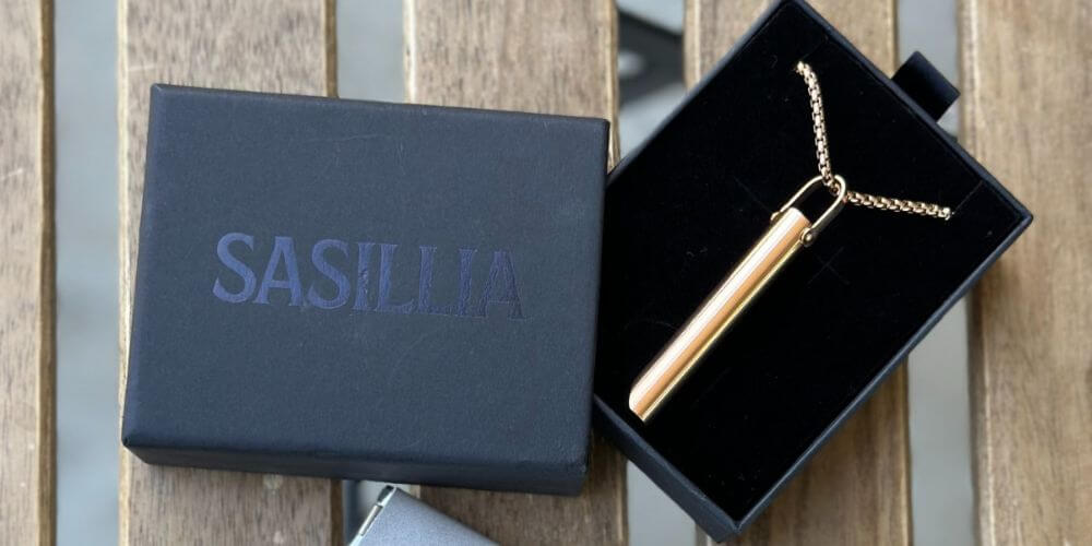 A gold pendant necklace inside a black Sasillia box on a wooden surface.