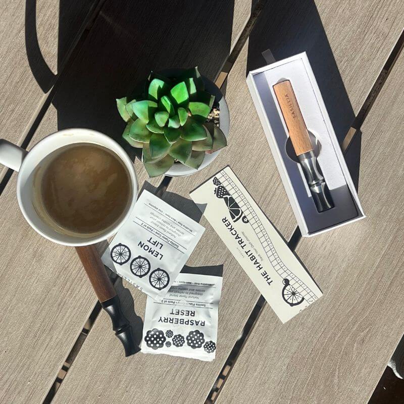 Coffee cup, succulent, tea packets, habit tracker, and boxed tool on wooden table.
