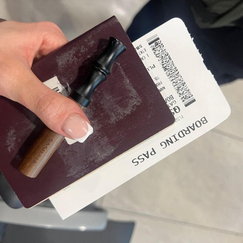 Hand holding a boarding pass, passport, and a small cylindrical item.