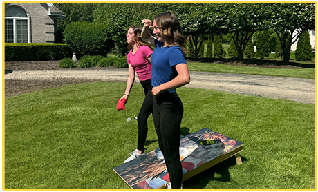 Two people playing cornhole on a lawn on a sunny day.