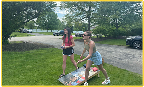 Two people playing cornhole outside on a sunny day.