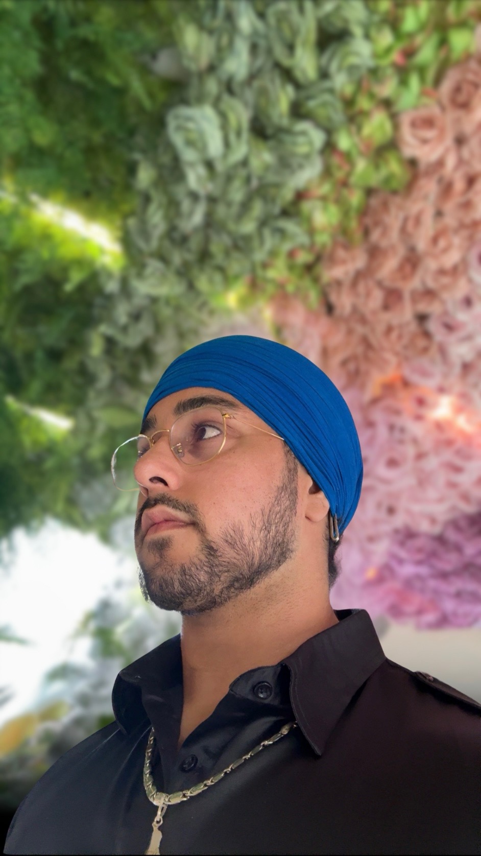 Person wearing a blue turban and glasses, with a floral background.