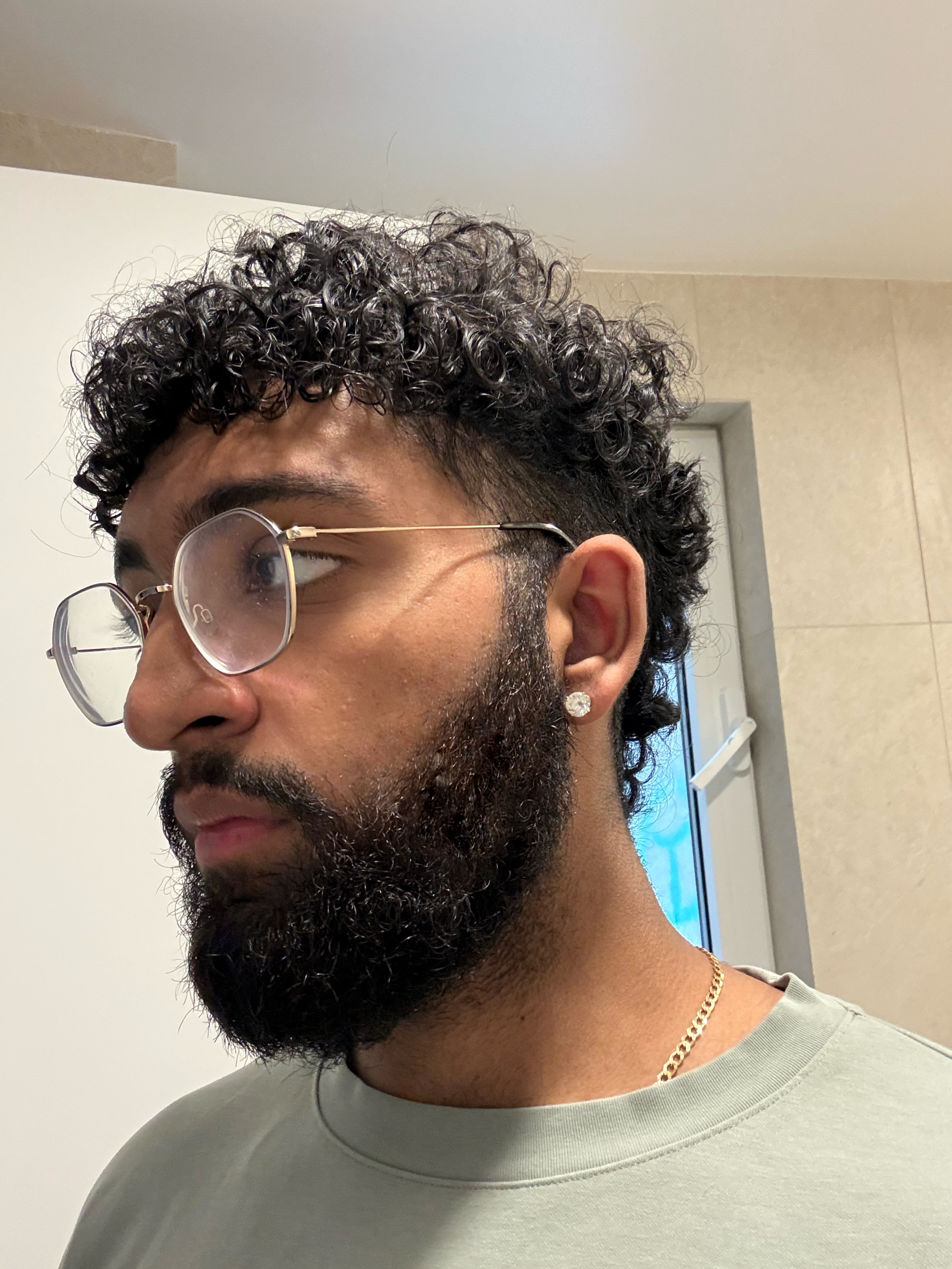 Person with curly hair, glasses, and a beard in a room with a window.