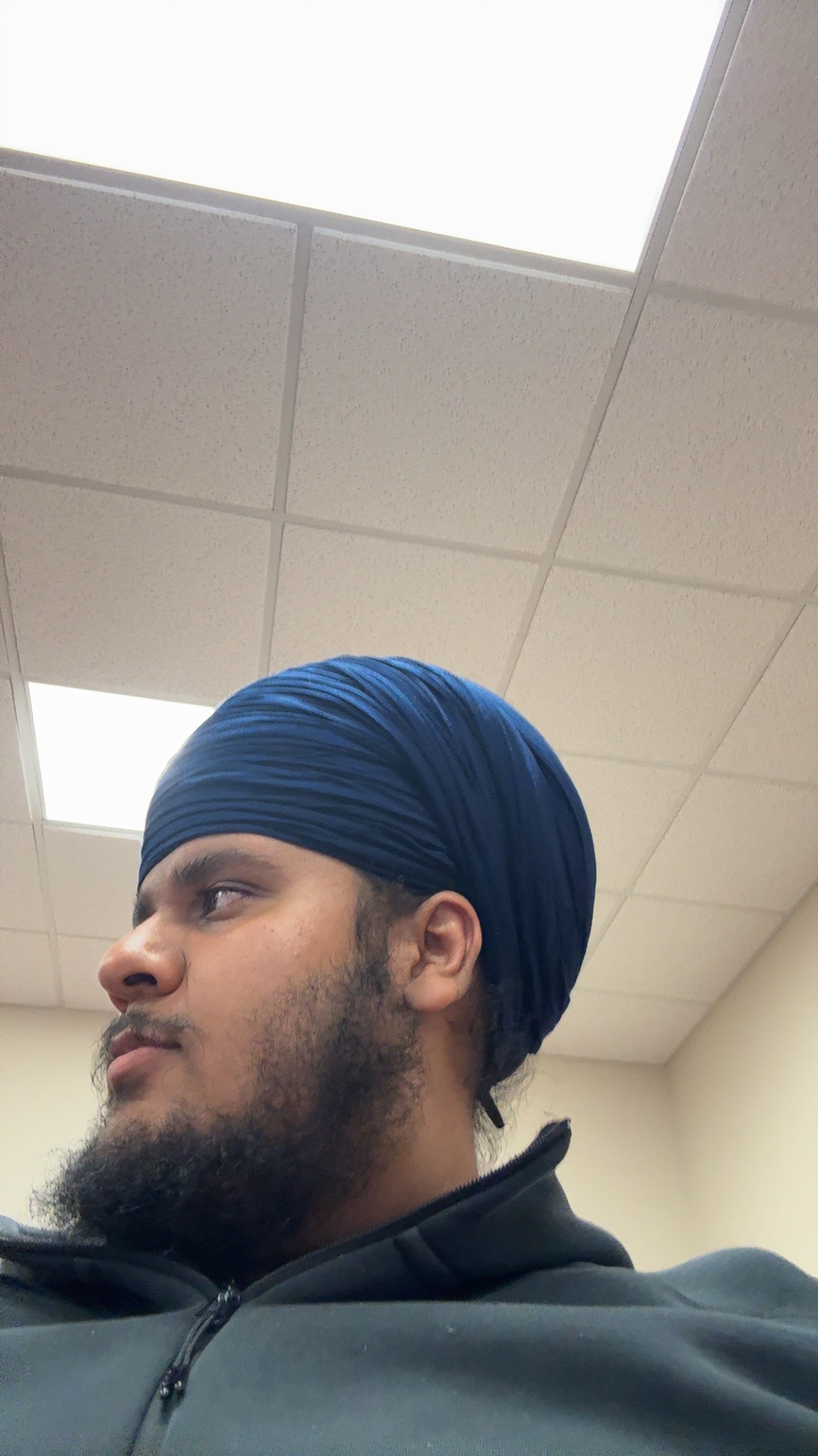 Person wearing a blue turban in a room with ceiling tiles.