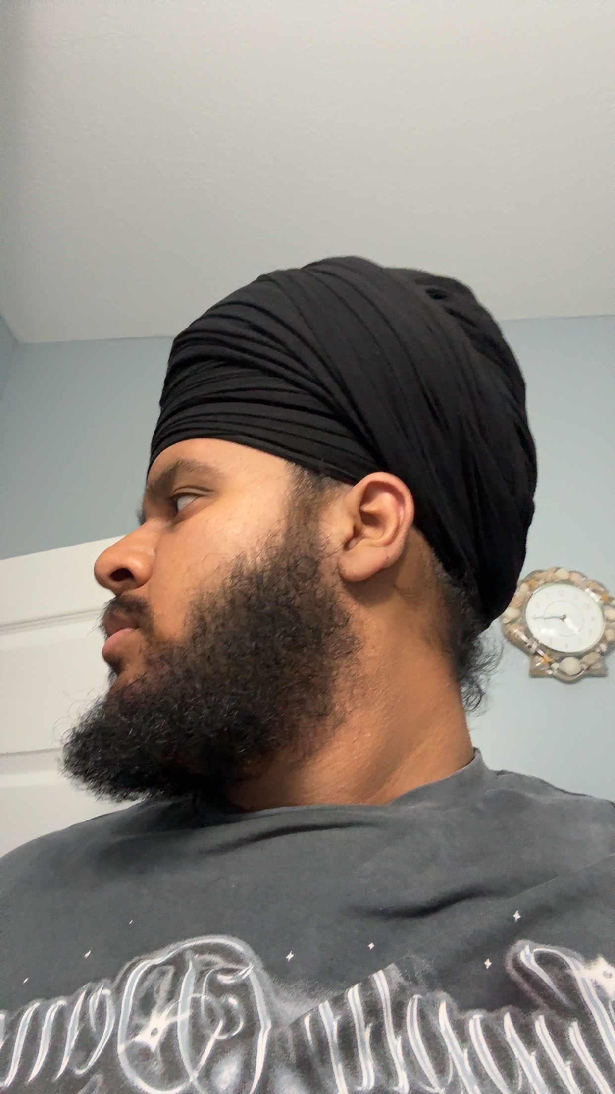 Person with a black turban looking sideways, wall clock in background.