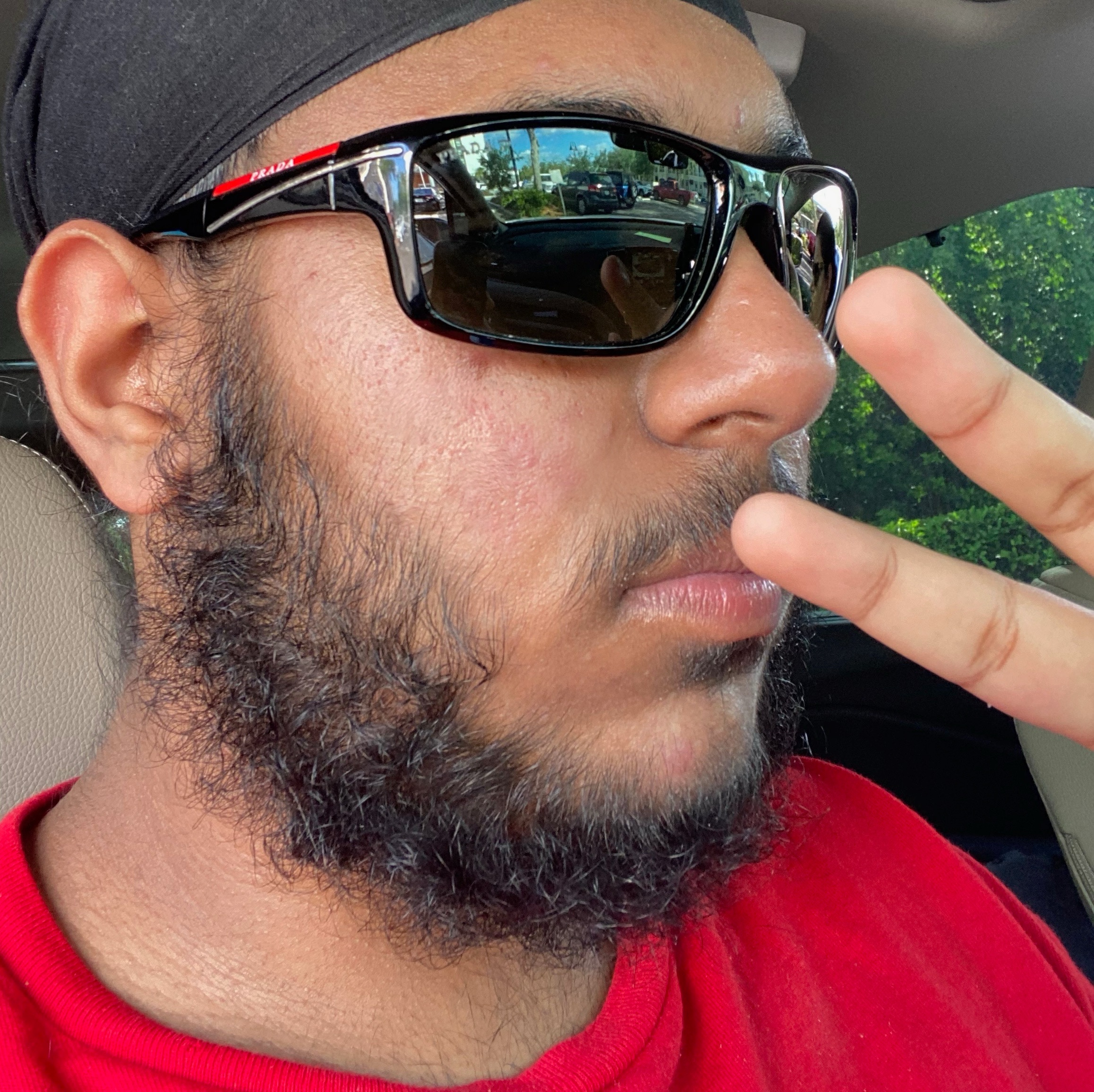 Person in sunglasses and a red shirt making a peace sign in a car.
