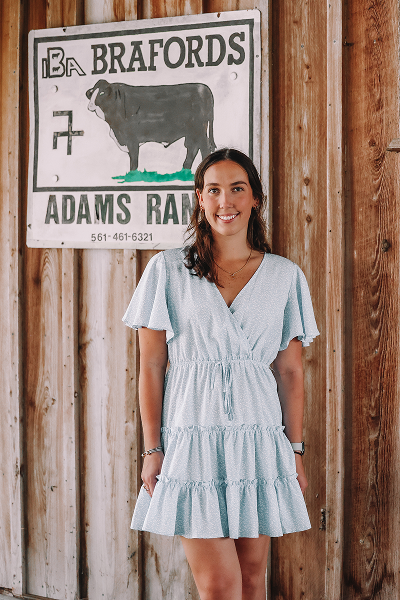 Person in light dress standing by a wooden wall with a ranch sign.