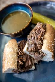 Two beef sandwiches with au jus dip and a pickle on a blue plate.