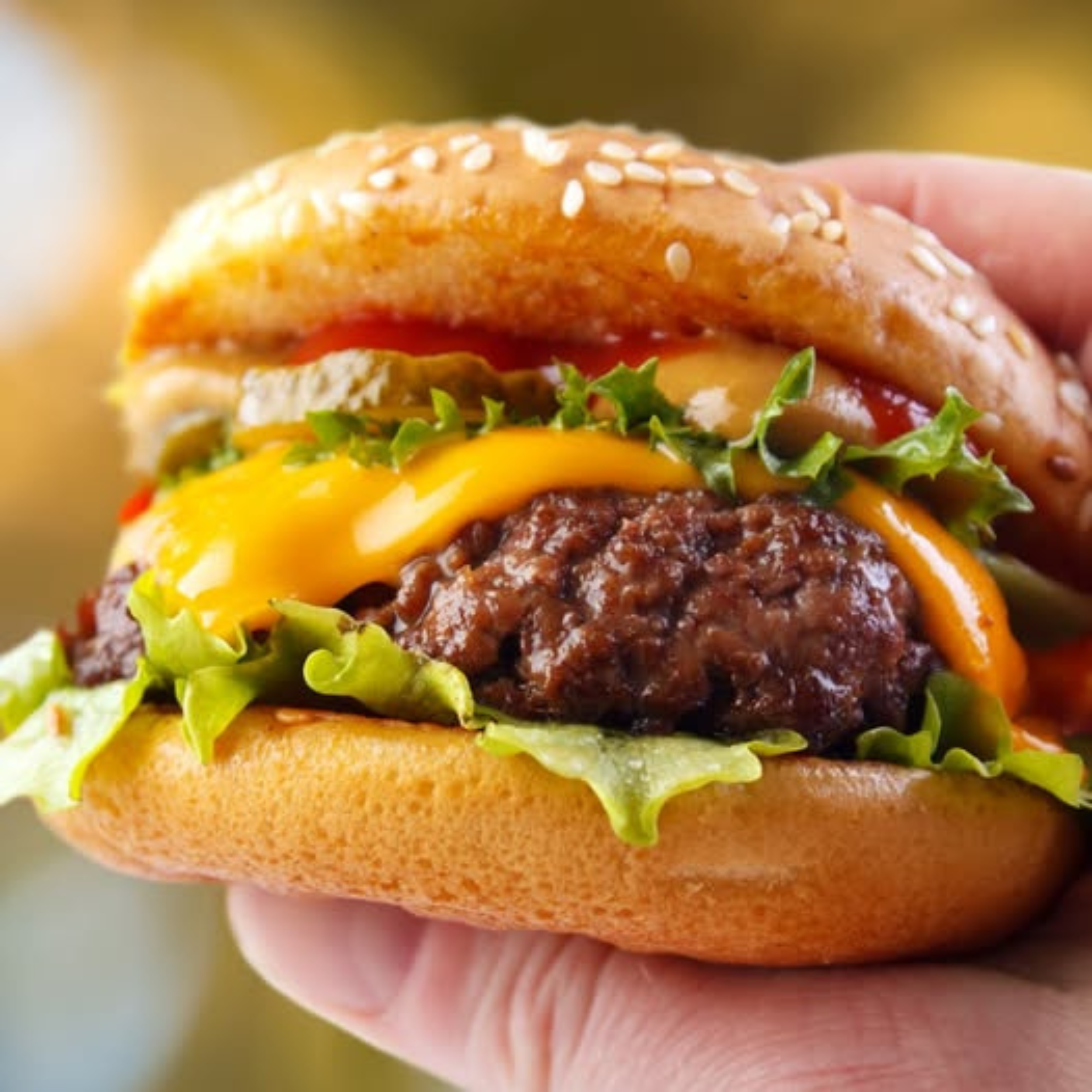 A close-up of a hand holding a cheeseburger with a sesame seed bun, lettuce, and melted cheese.