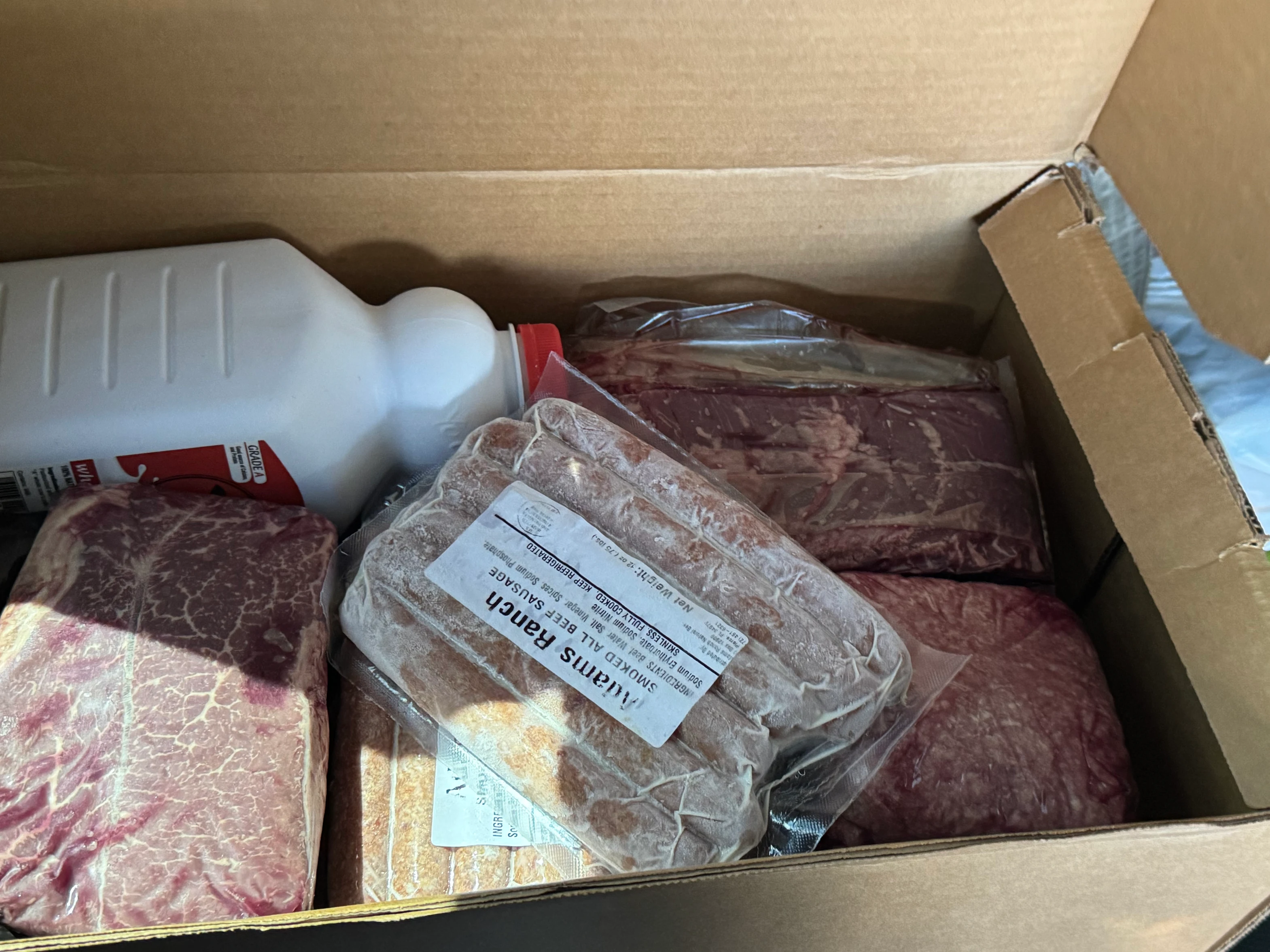 Box containing various packaged meats and a white bottle.