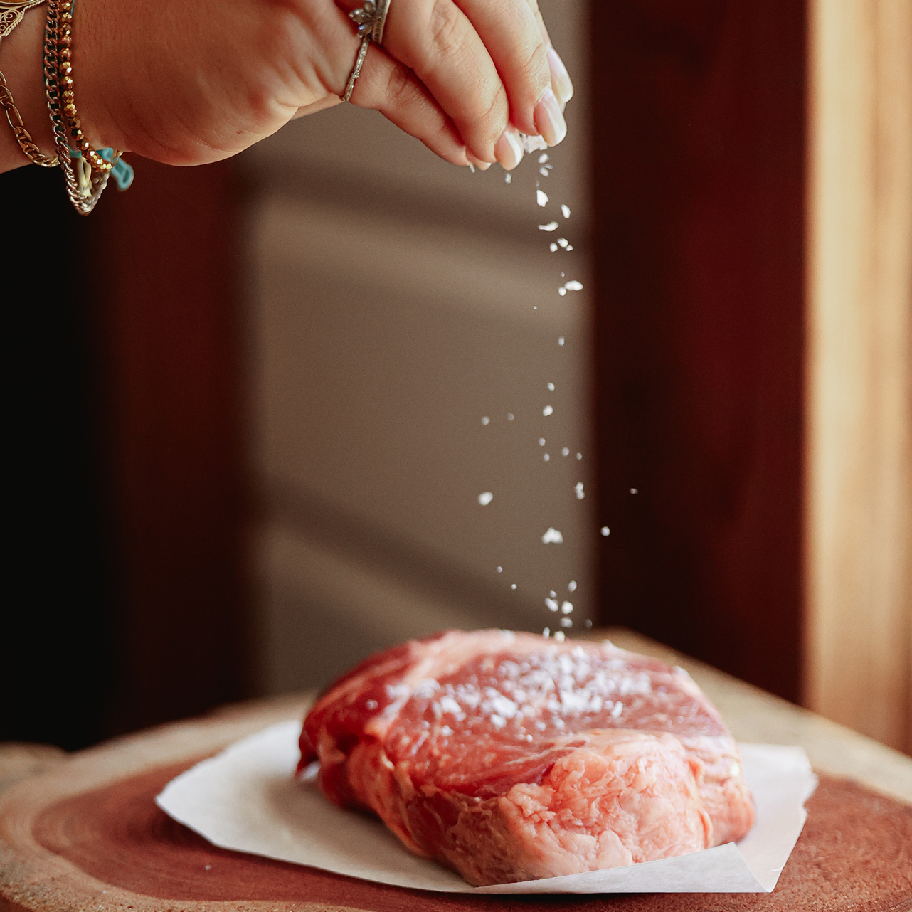 Person seasoning a raw piece of meat with salt flakes.