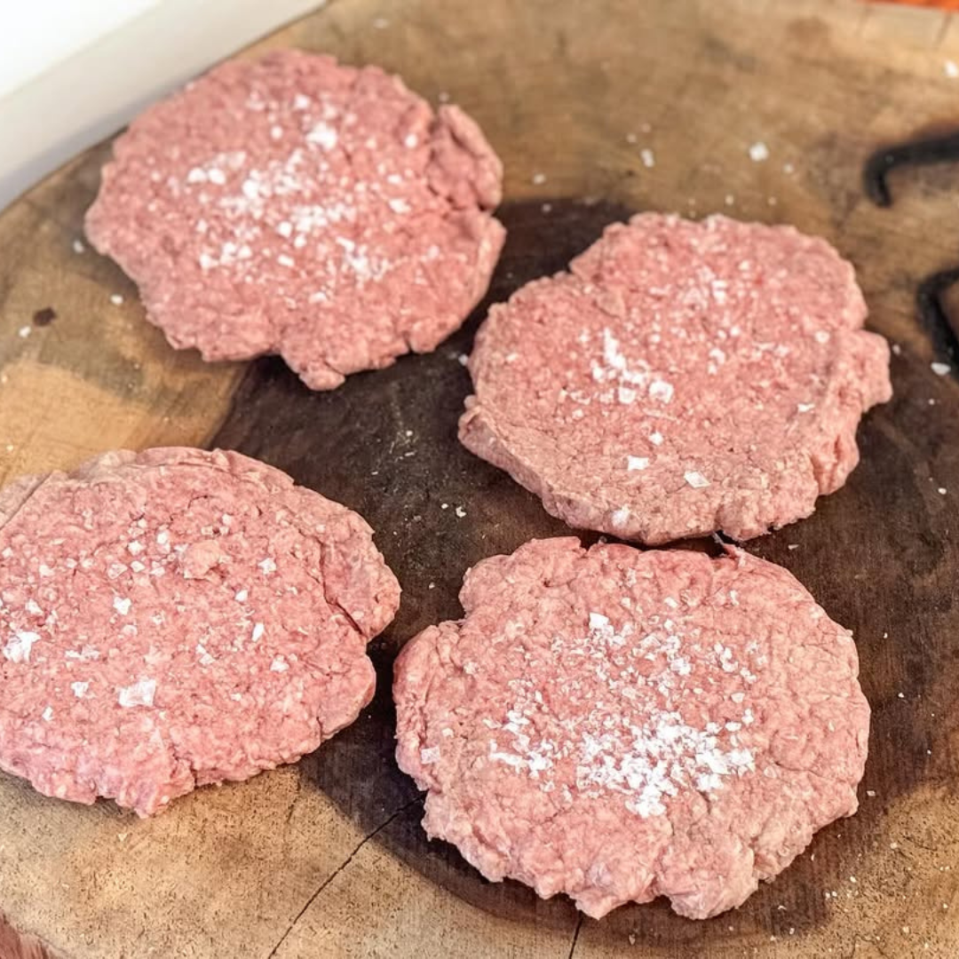Four raw burger patties on a wooden cutting board.
