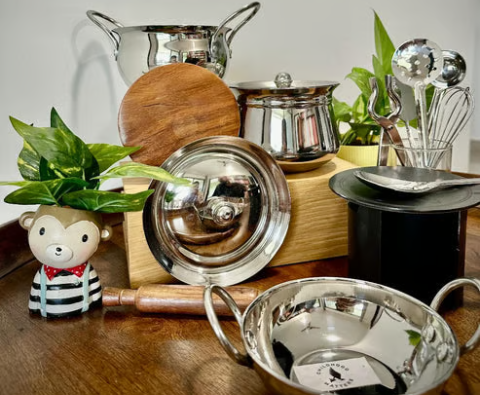Assorted kitchen items, including pots, pans, plants, and a bear figurine, on a wooden surface.