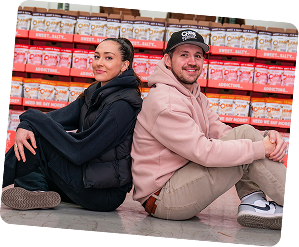 Two people sitting back-to-back in front of stacked snack boxes.