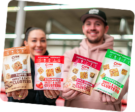 Two people holding packets of snack clusters in various flavors.