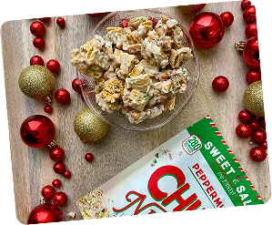 Bowl of snack mix on a table with holiday decorations and a snack package.
