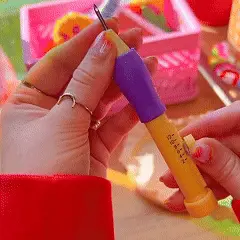 Person holding a yellow and purple crafting tool with a sharp tip.