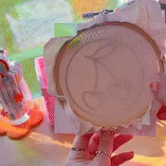Hand holding a circular embroidery hoop with a cherry design.