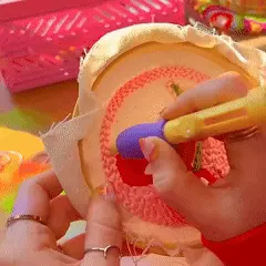 Person using a punch needle tool on fabric with colorful threads.