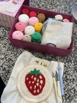 Box of colorful yarn and a strawberry embroidery on a table.