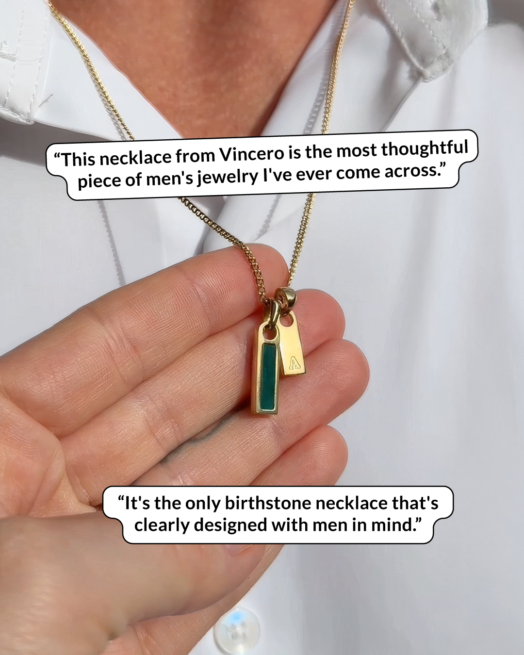 A hand holds up a gold necklace with a green stone pendant and a small initial tag.