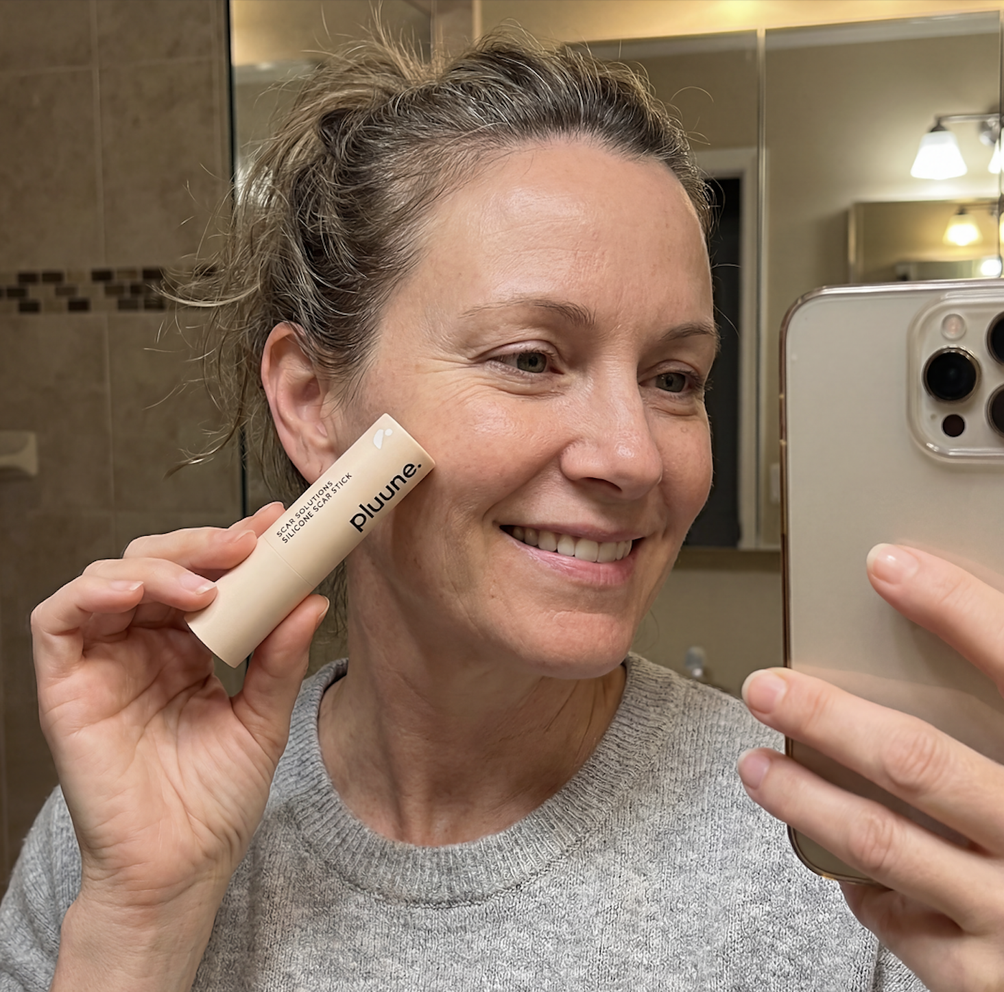 Woman smiling with skincare stick in bathroom.