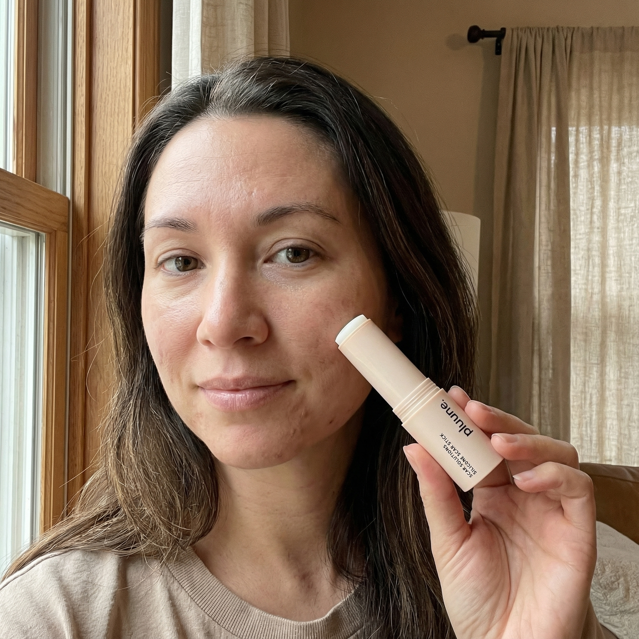 Person holding a cylindrical cosmetic product near their face.