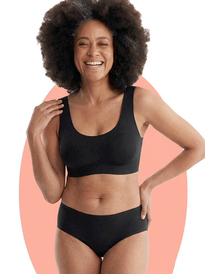 Person smiling in black two-piece outfit on a peach background.