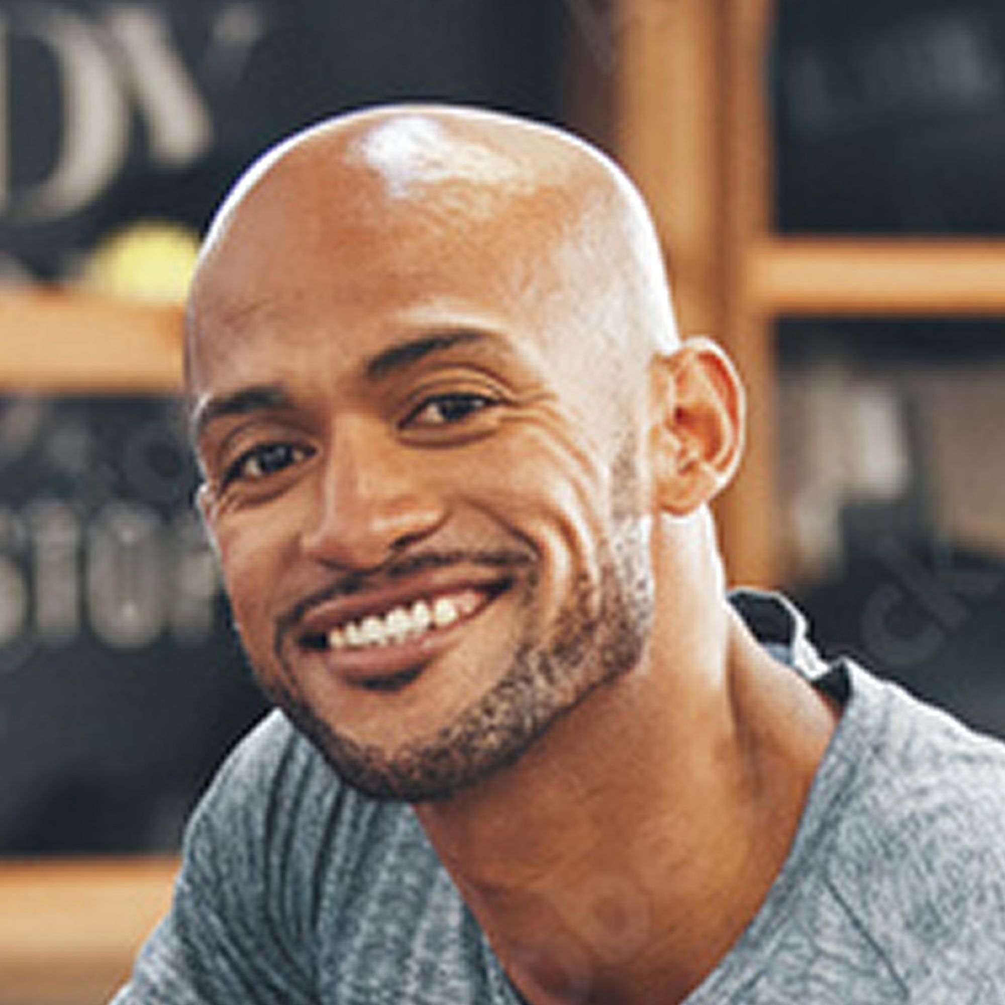 Smiling man with a shaved head and beard, wearing a gray shirt.
