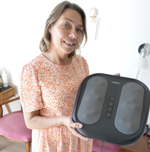 Woman in floral dress holds a foot massager in a living room.
