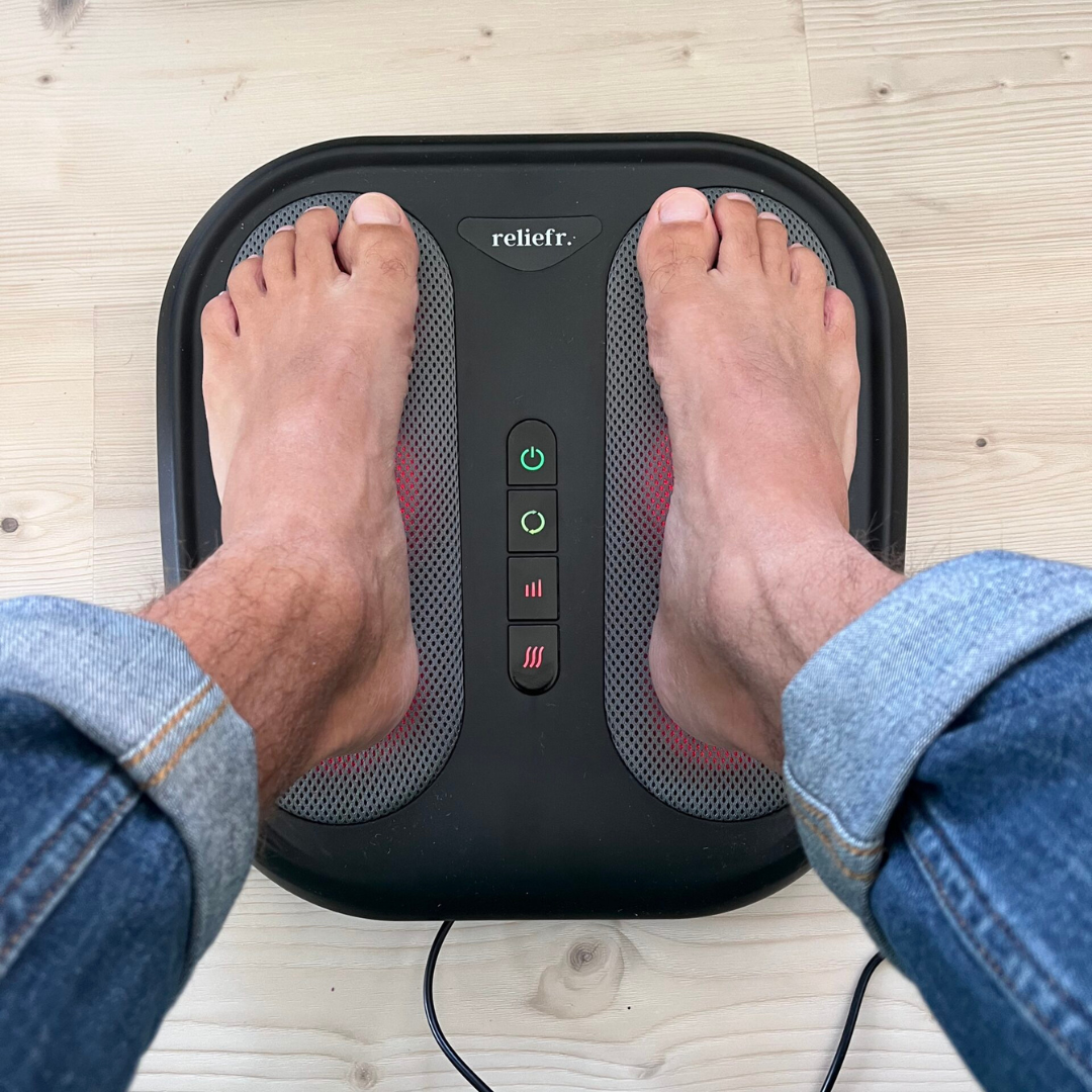 Two feet placed on an electronic foot massager on a wooden floor.