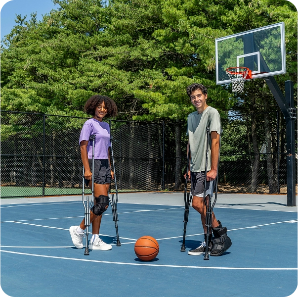 Two people on crutches with a basketball on an outdoor court.