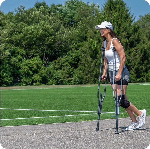 Person walking with crutches on a path next to a field.