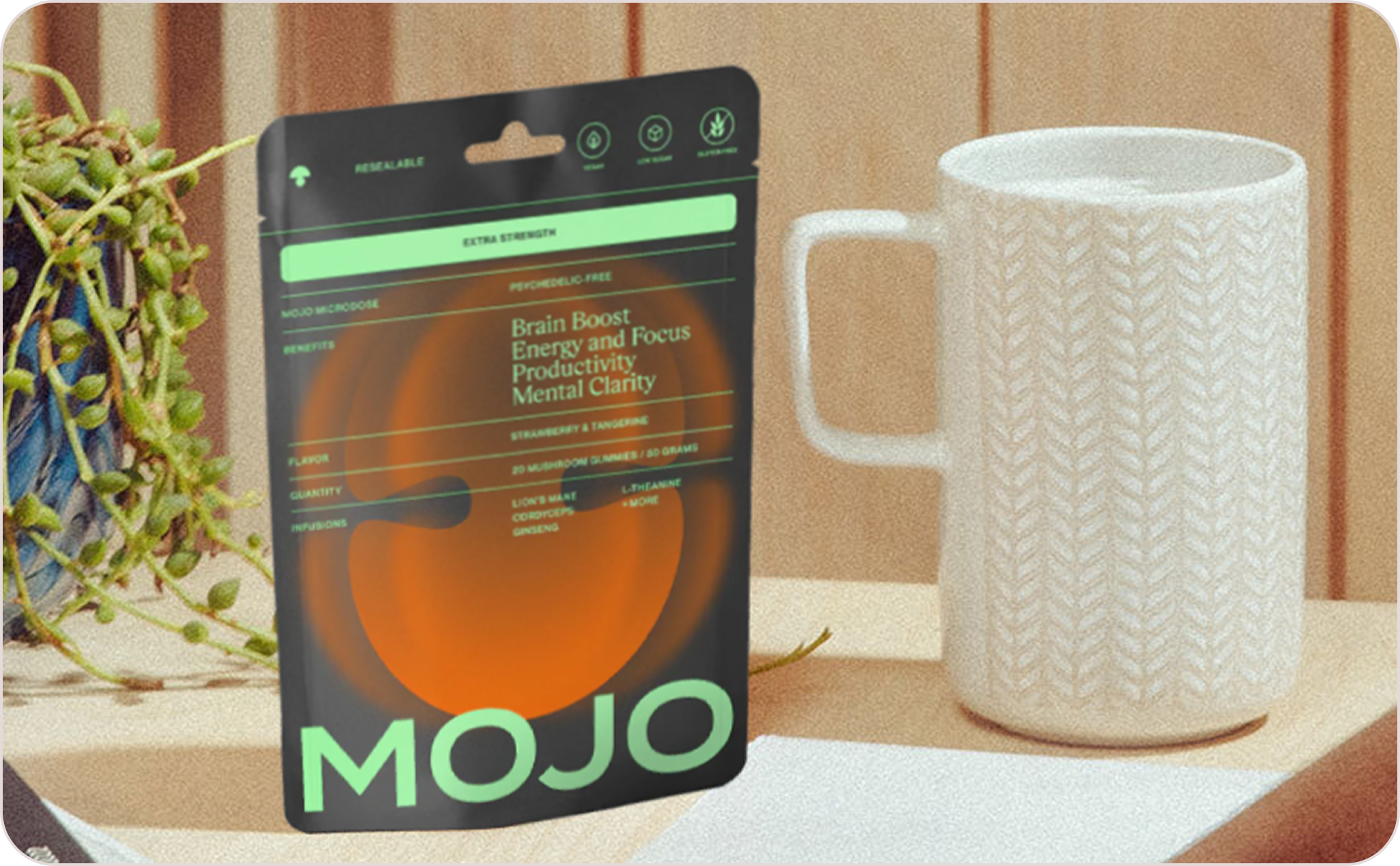 A packet labeled 'MOJO' next to a white textured mug and a plant.
