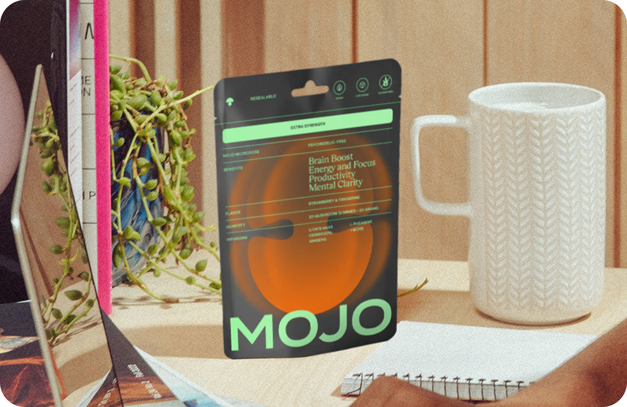 A packet labeled 'MOJO' next to a white mug and plant on a table.