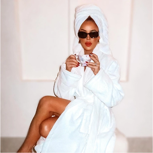 Person in a white robe and towel, wearing sunglasses, holding a teacup.