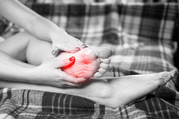 A person's hands massaging the bottom of their foot, with a red highlight indicating a painful area.