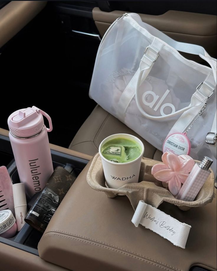 Car seat with a white bag, pink bottle, and green drink.