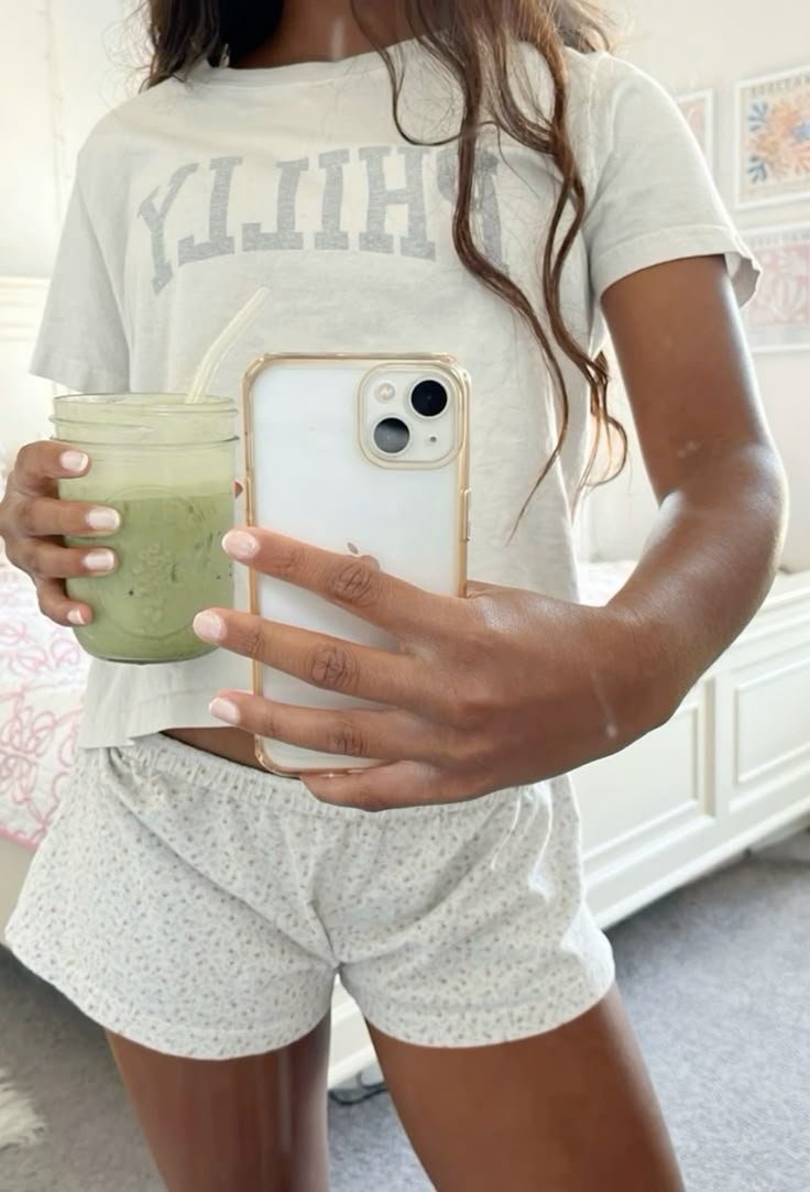 Person holding a phone and a green smoothie in a bedroom.