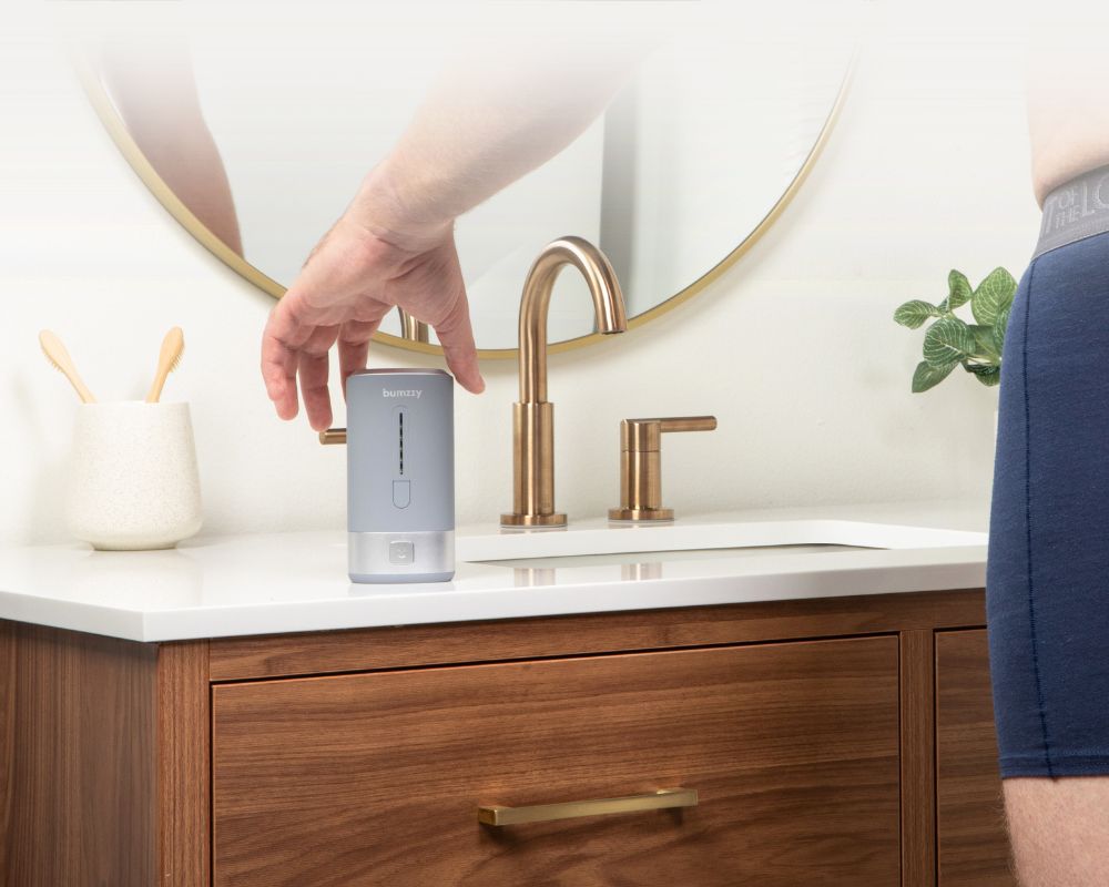 Person using a device on a bathroom counter with a faucet and mirror.