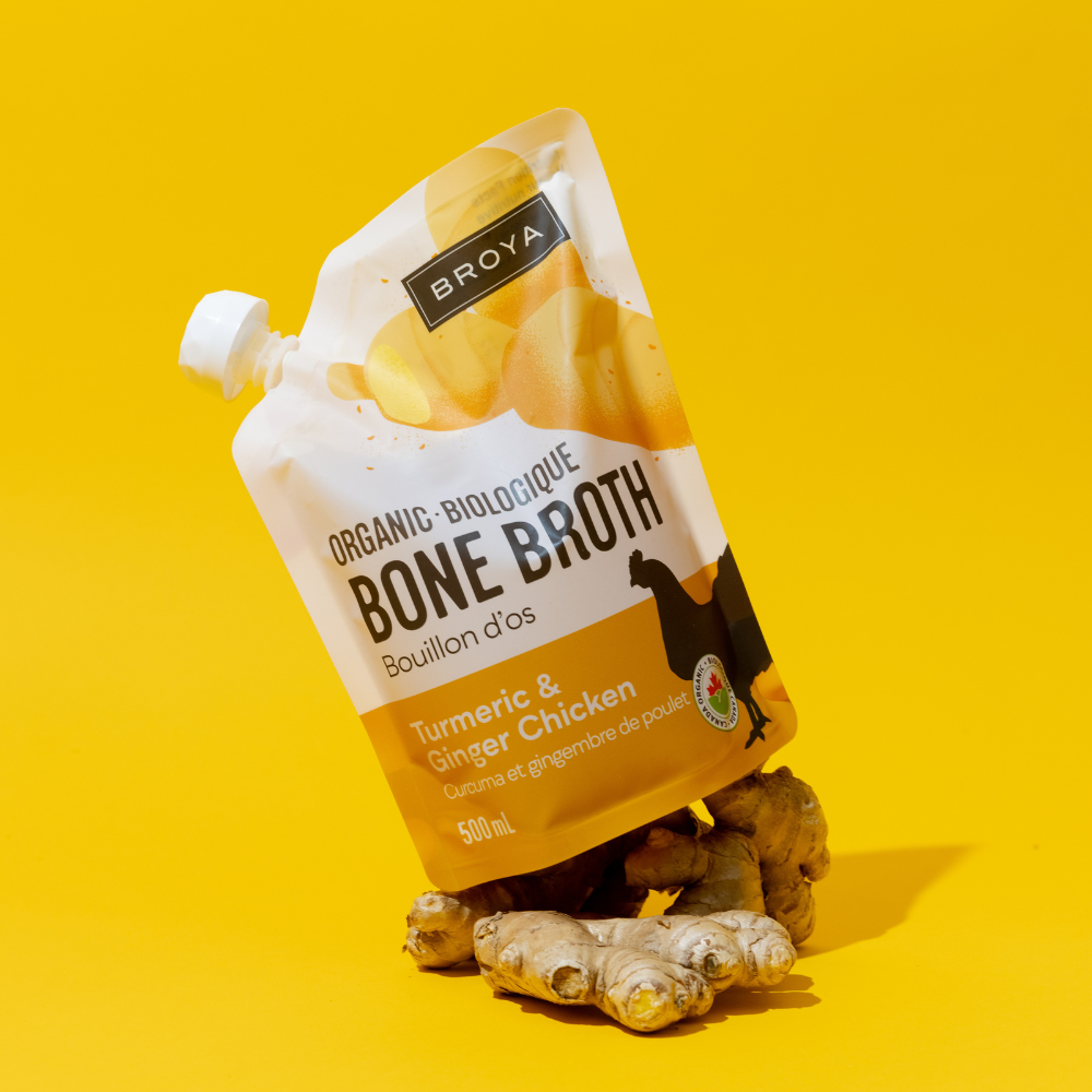 Pouch of organic bone broth on ginger roots, yellow background.