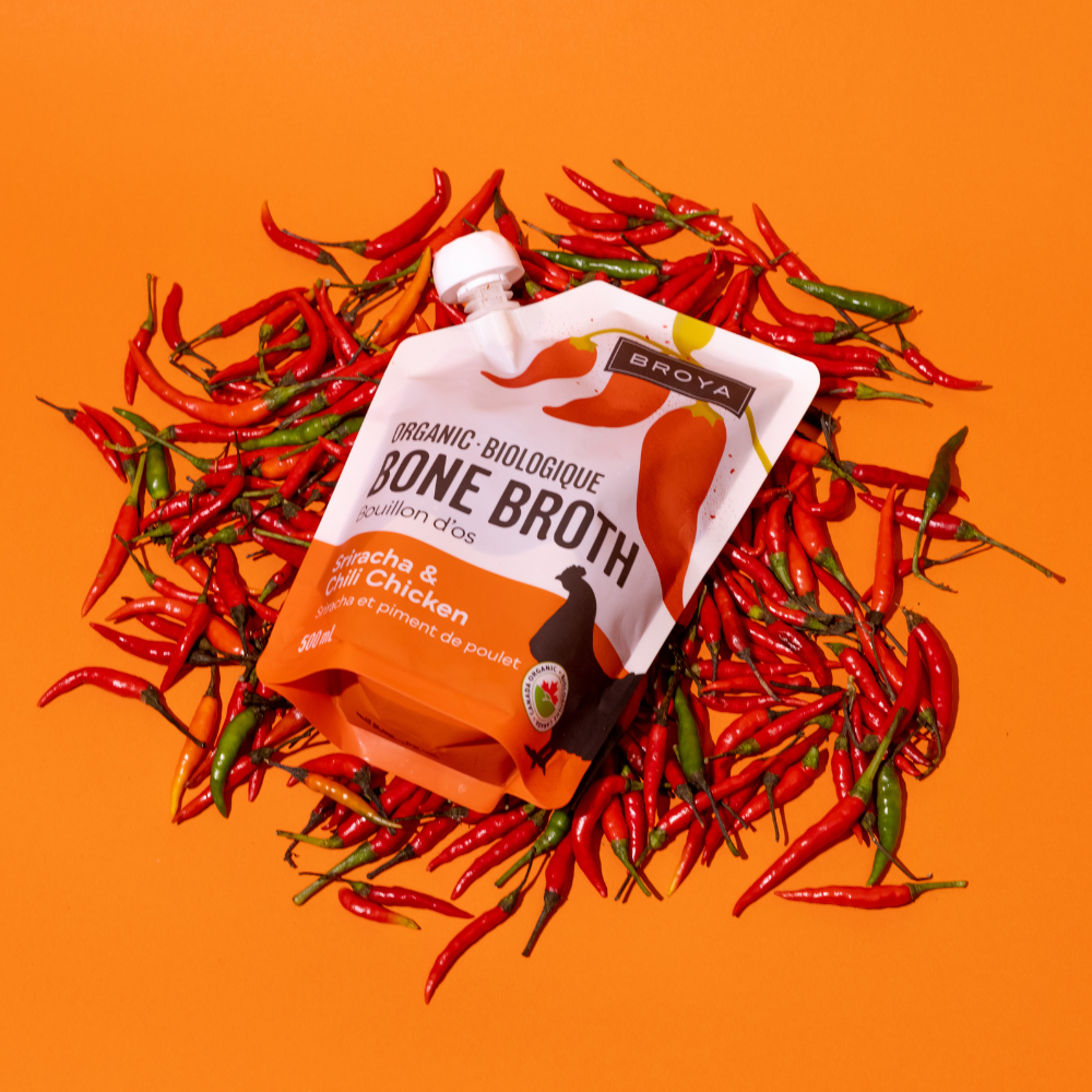 Pouch of bone broth surrounded by red and green chili peppers on orange background.