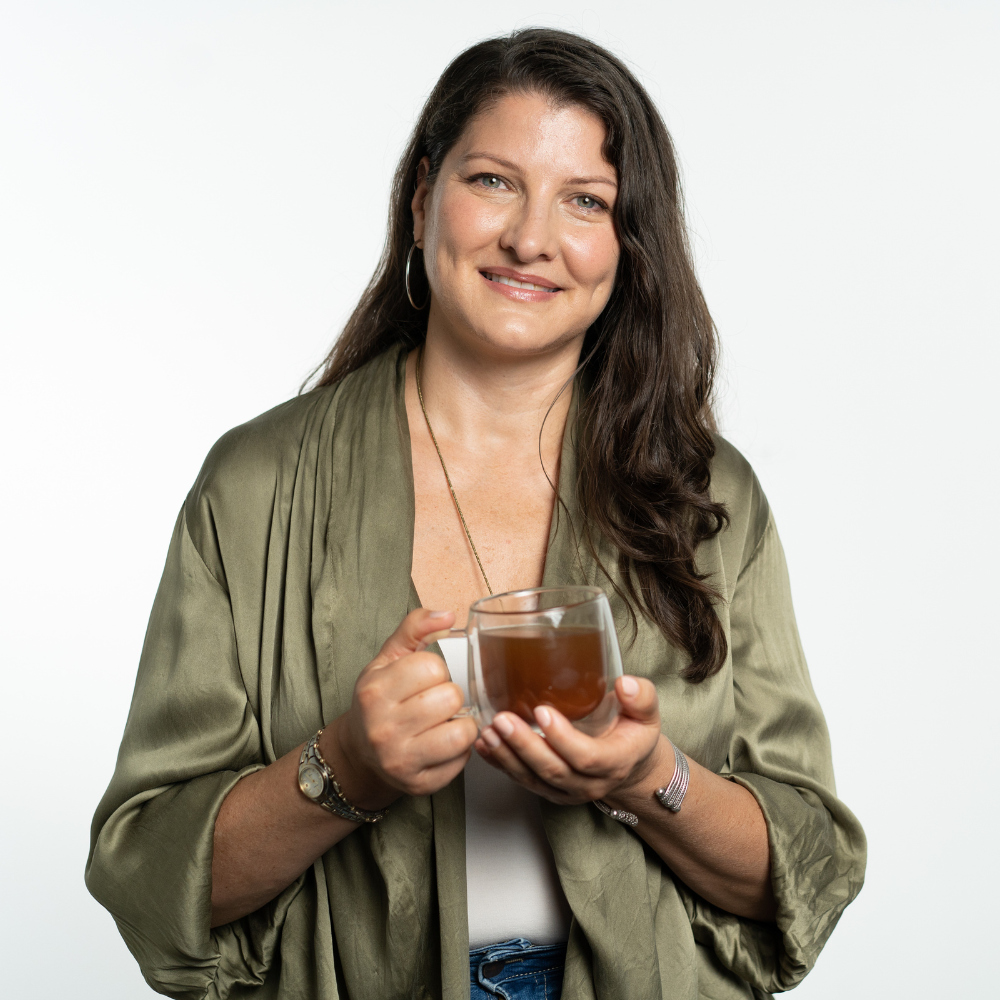 Woman in green robe holding a glass mug with tea, smiling.