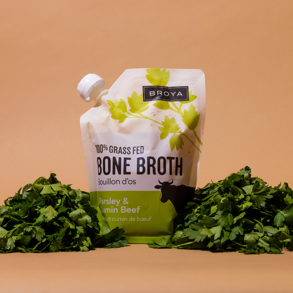 Broya bone broth pouch surrounded by fresh parsley on a brown background.