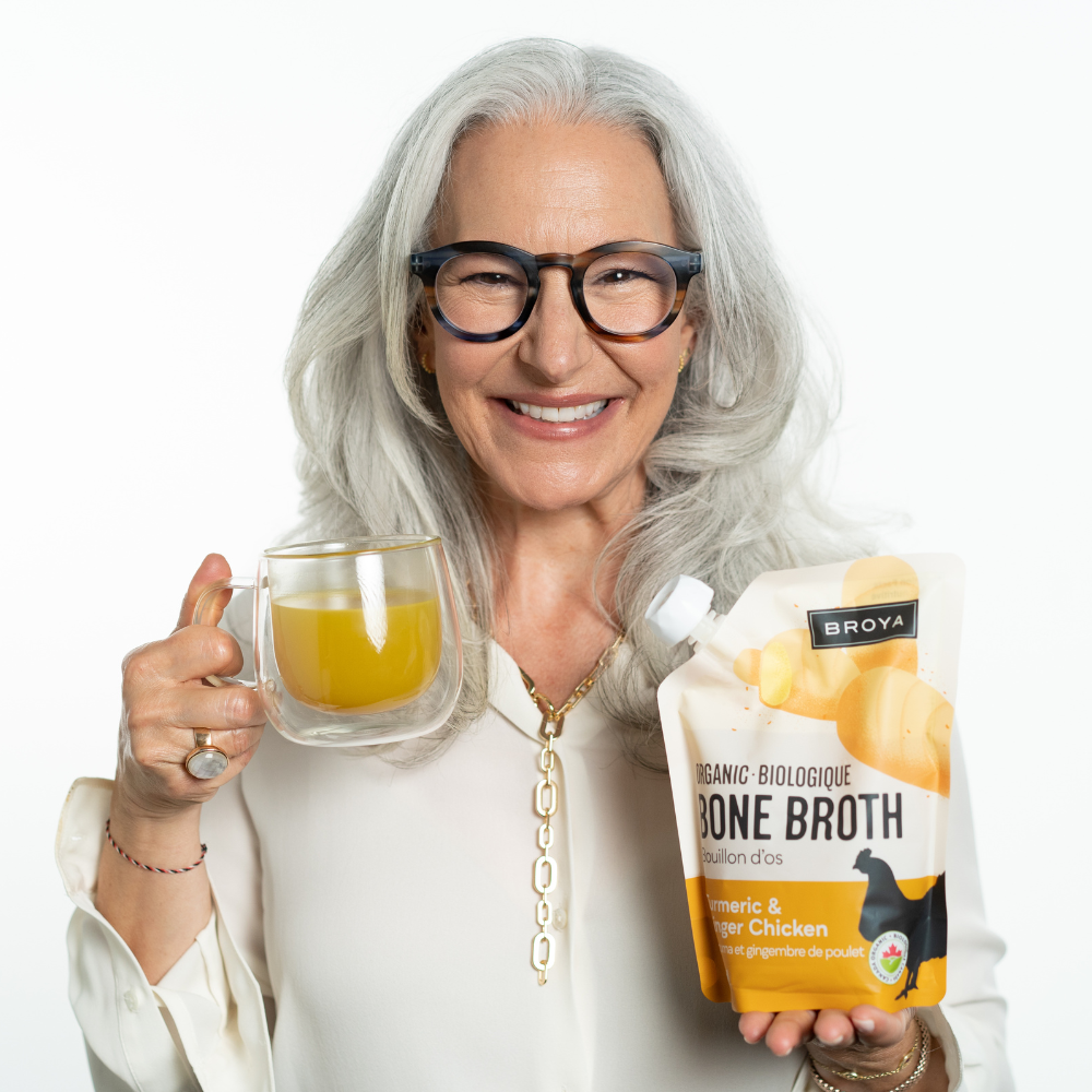 Smiling woman holding a glass of broth and a bone broth package.