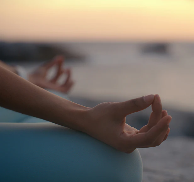 Person meditating with hands in mudra against a sunset background.