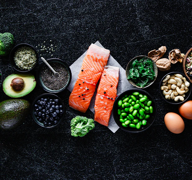 Assorted healthy foods including salmon, nuts, berries, and vegetables on a dark surface.